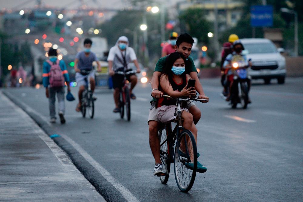 FILE PHOTO: A cyclist carries a passenger wearing a protective face mask, amid the coronavirus disease (Covid-19) pandemic, in Manila, Philippines, June 11, 2021. -Reuters