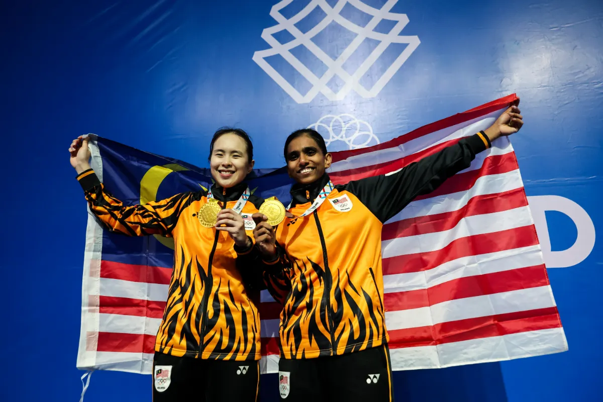 Malaysian women's doubles players Pearly Tan and M. Thinaah show off the gold medal they won in the 2025 SEA Games badminton final at Gymnasium 4, Thammasat University, Rangsit Campus.