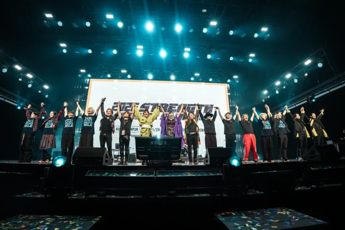 The full lineup of performers, including the accompanying band and backstage crew, appears together on stage during the show.