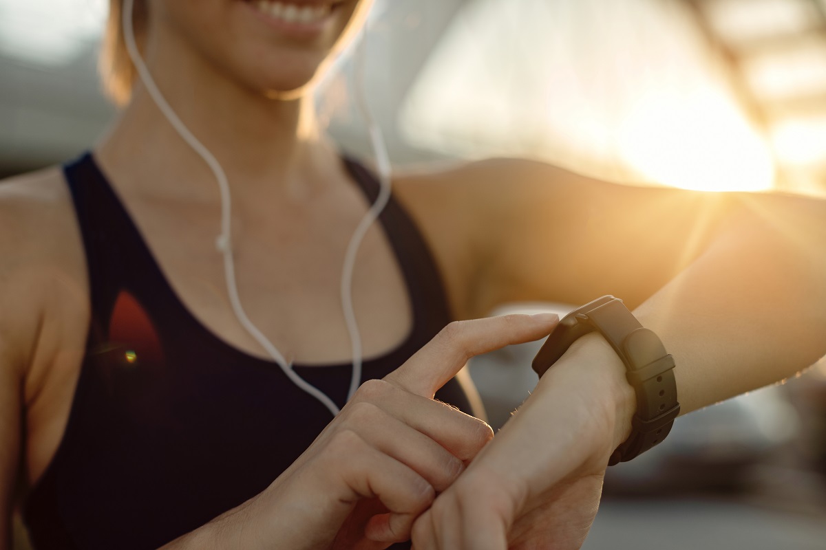 Close-up of athletic woman using fitness tracker at sunset. Are smartwatches accurate for health tracking?
